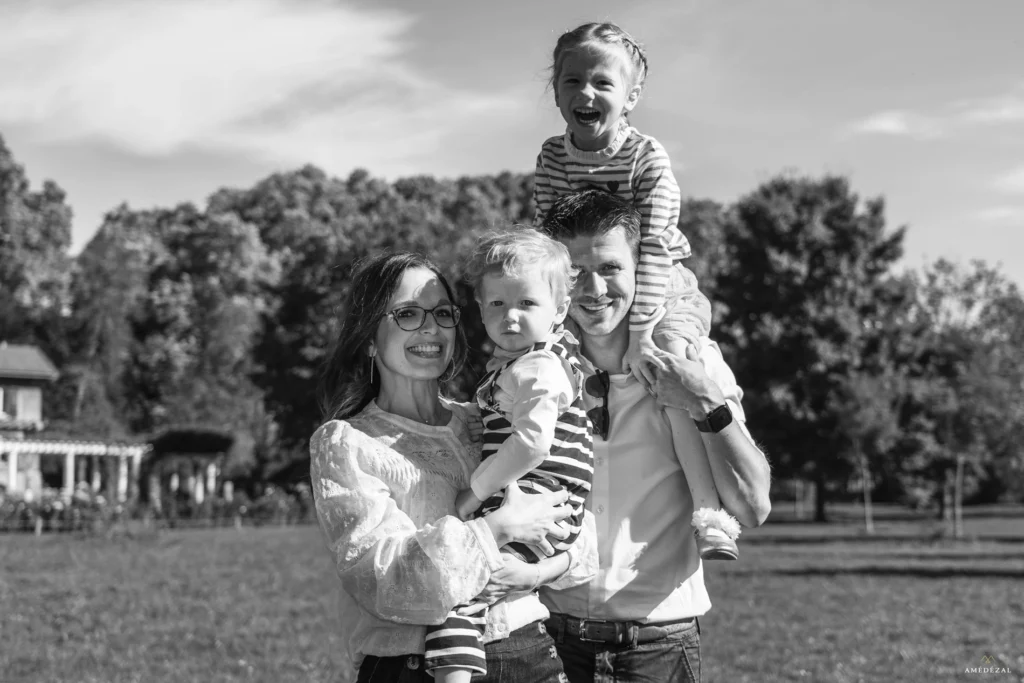 Portrait en noir et blanc d'une famille souriante dans un parc, père portant sa fille sur les épaules, photographe Amedezal Auvergne-Rhône-Alpes