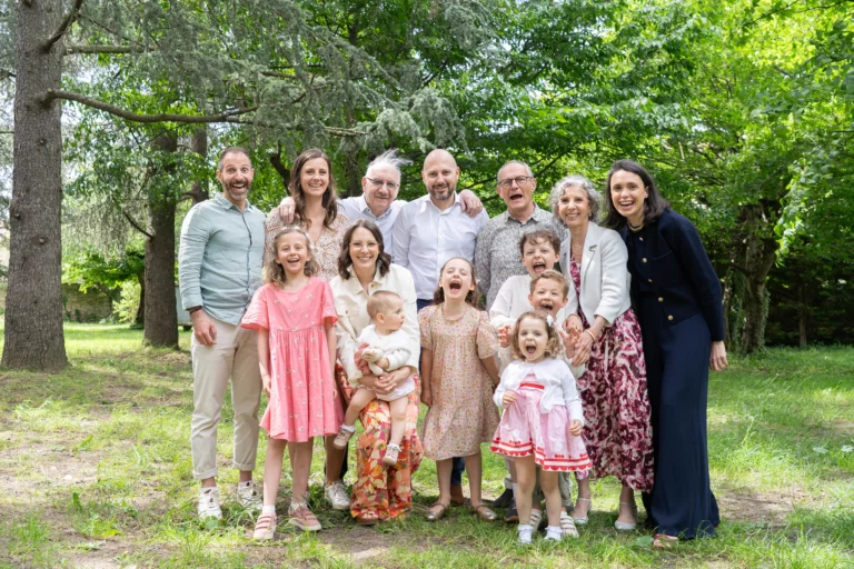 Portrait joyeux d'une famille élargie sur trois générations en extérieur lors d'un baptême, enfants et adultes qui rient, photographe Amédézal à Lyon