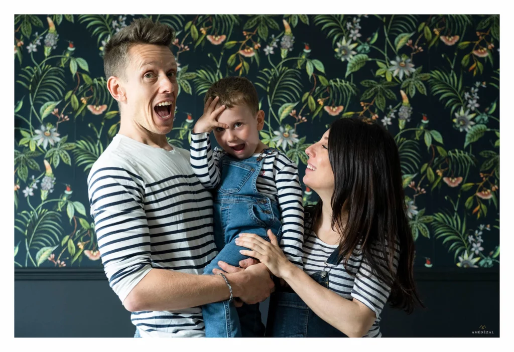 Papa faisant une grimace avec son enfant dans les bras lors d'une séance photo famille en appartement à Vaugneray, photographe Amédézal