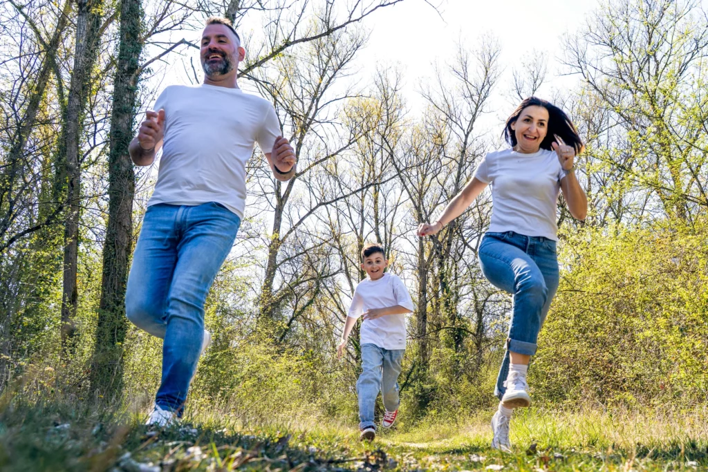 Parents et enfant qui courent en riant dans un bois lors d'une séance photo famille lifestyle en Auvergne-Rhône-Alpes