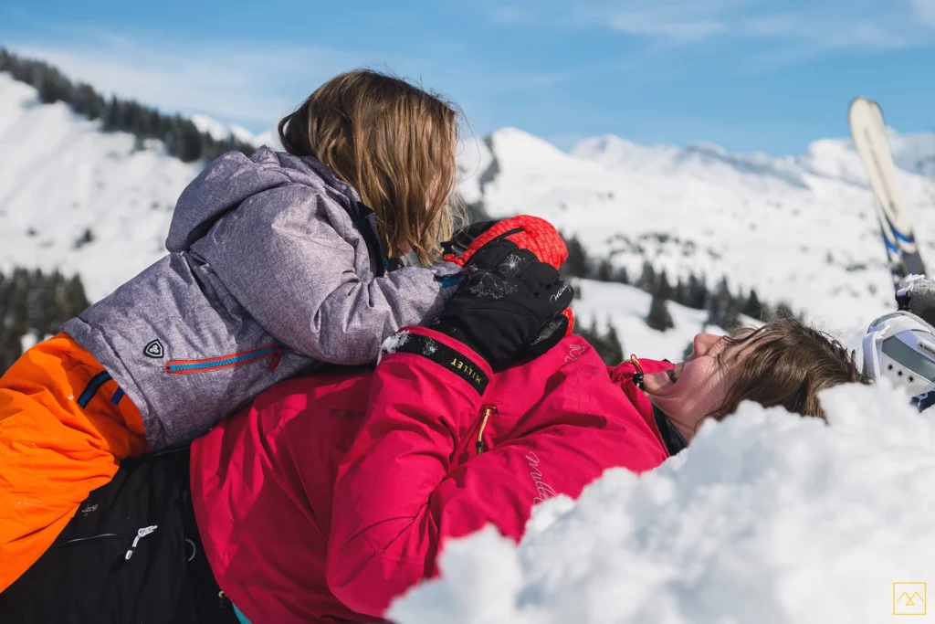 Enfant grimpant sur sa maman allongée dans la neige en montagne, séance photo famille lifestyle par Amedezal en Auvergne-Rhône-Alpes